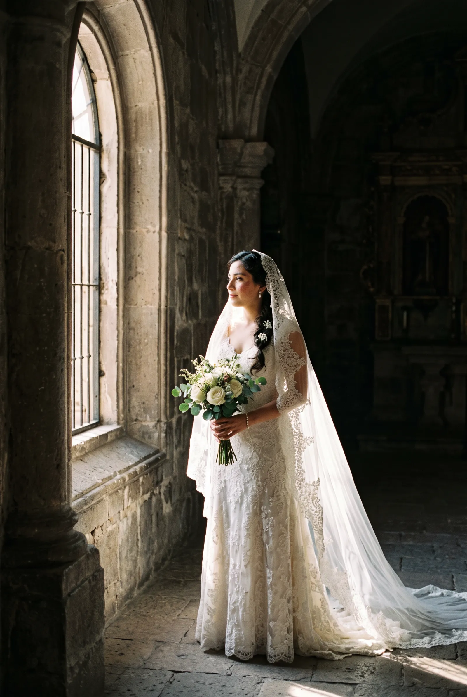 Novia de pie dentro de una iglesia de piedra con el velo iluminado a contraluz
