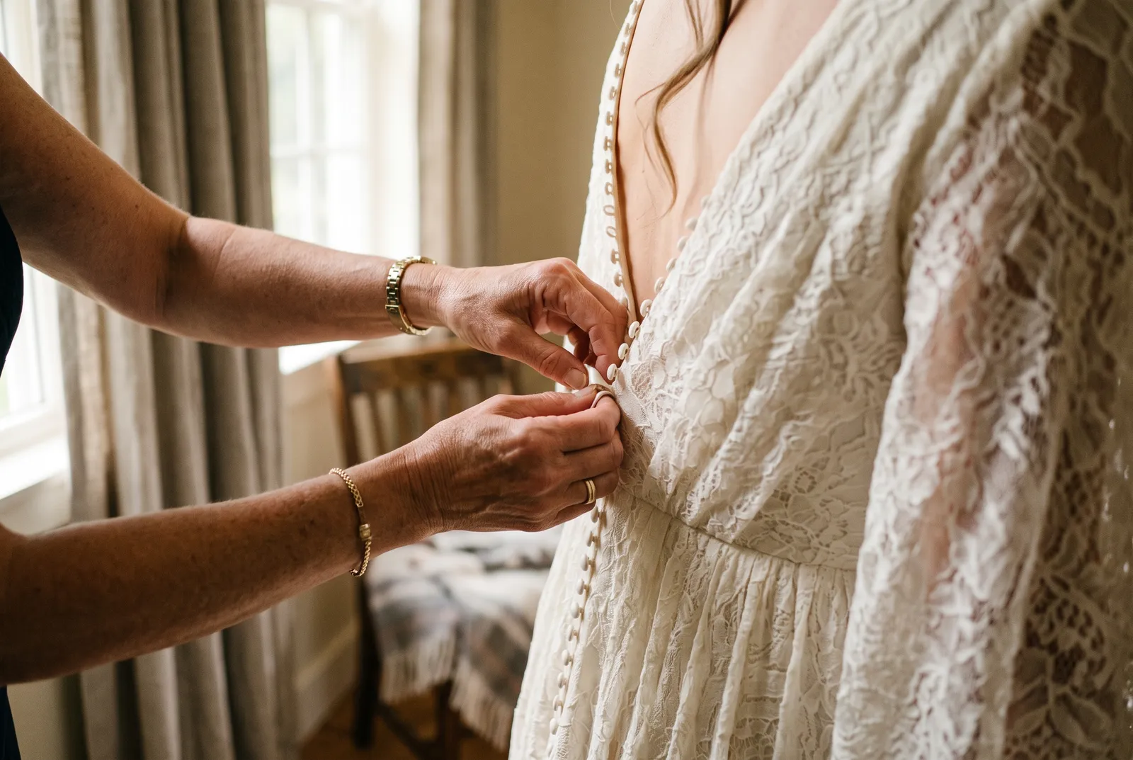 Manos abrochando los botones traseros de un vestido de novia color marfil